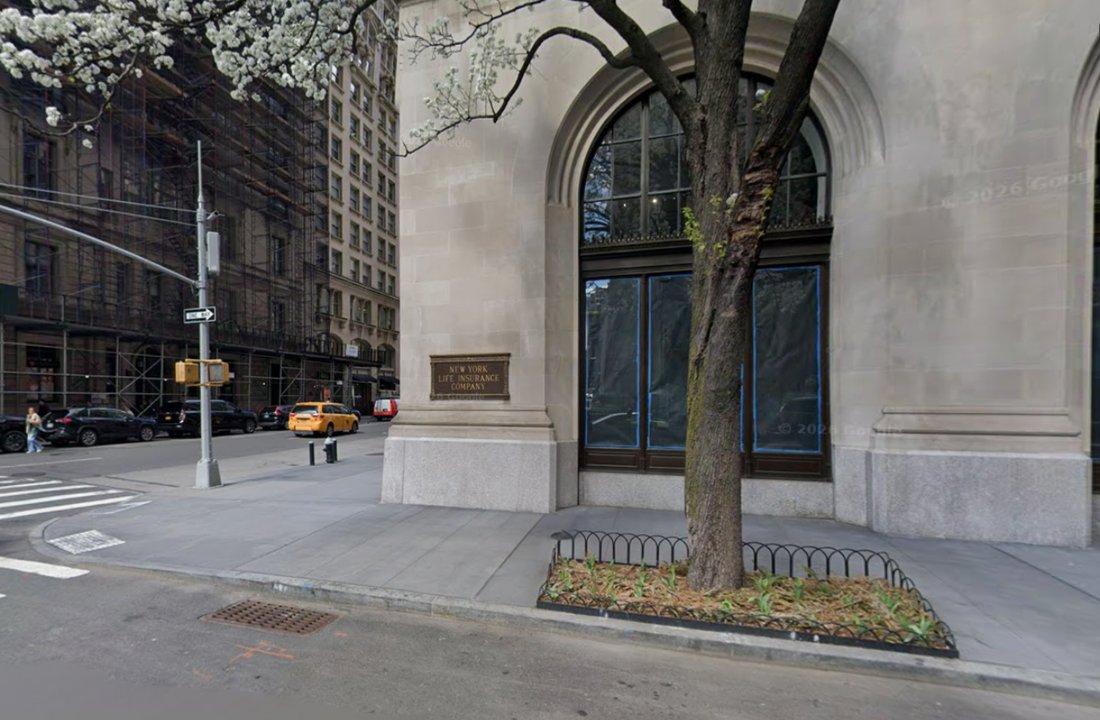 City street corner with a large stone building featuring an arched window and a sign reading “New York Life Insurance Company.” A tree stands in front, and cars, including a yellow taxi, are visible along the street.