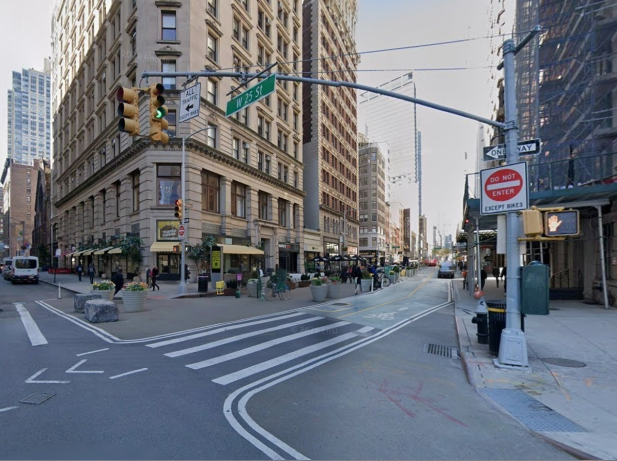 City street intersection with traffic lights, street signs, and pedestrians in an urban setting.