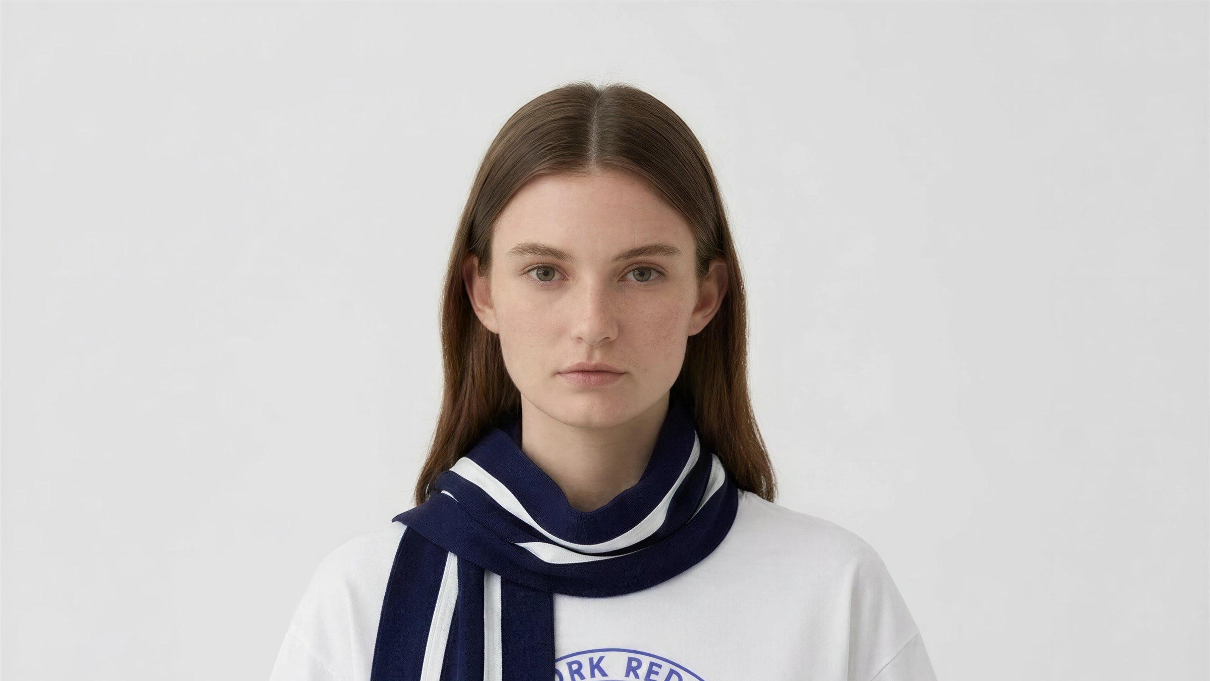 Woman wearing a white sweatshirt with a blue and white scarf, on a plain background